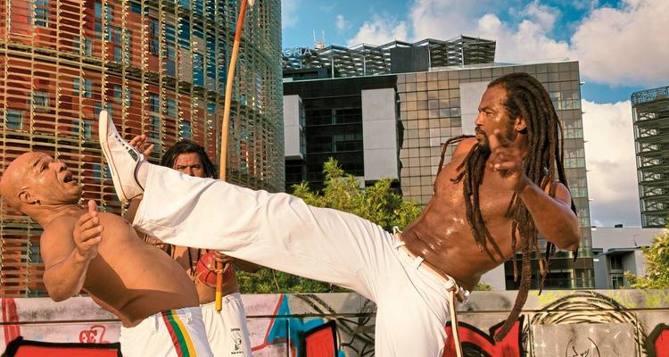 Capoeira-Künstler führen eine hochenergetische Tritttechnik vor einem farbenfrohen urbanen Hintergrund in Brasilien auf.
