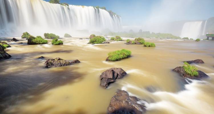 Die mächtigen Iguazu-Wasserfälle stürzen in eine neblige Schlucht ab, wobei braunes Flusswasser um felsige Inseln wirbelt.