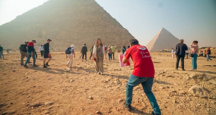 Un guide photographie un visiteur devant les pyramides imposantes tandis que d'autres touristes explorent le site.
