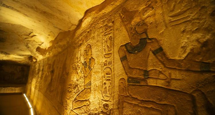 Couloir illuminé d'un tombeau égyptien antique avec des reliefs hiéroglyphiques détaillés gravés dans les murs de grès.