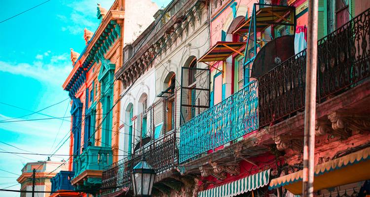Row of brightly painted balconies and façades in the historic La Boca neighborhood under a blue sky.