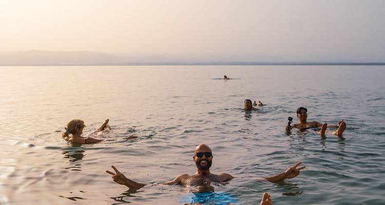 Travellers float effortlessly on the calm, mineral-rich waters of the Dead Sea under hazy evening light.