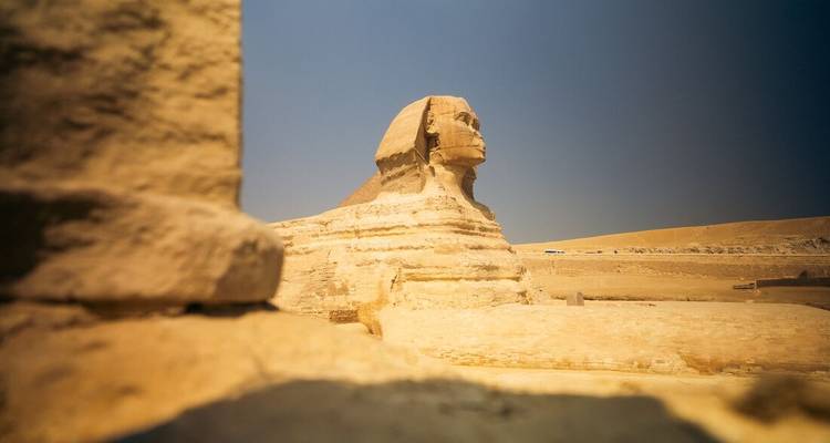 Side profile of the Great Sphinx of Giza framed by sun-baked stone blocks under a cloudless sky.