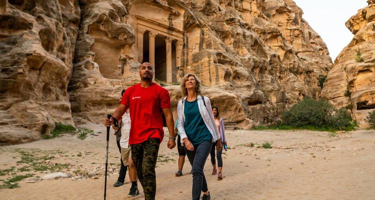Hikers make their way past towering sandstone cliffs toward a carved façade in Petra’s desert canyon.
