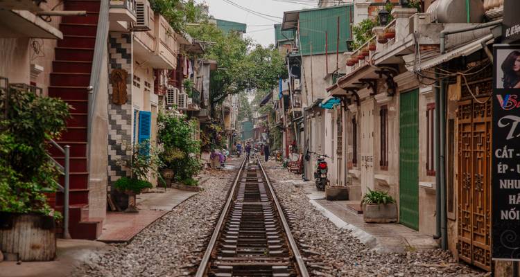 Iconic Hanoi Train Street with railway tracks running straight through narrow residential buildings and cafes.