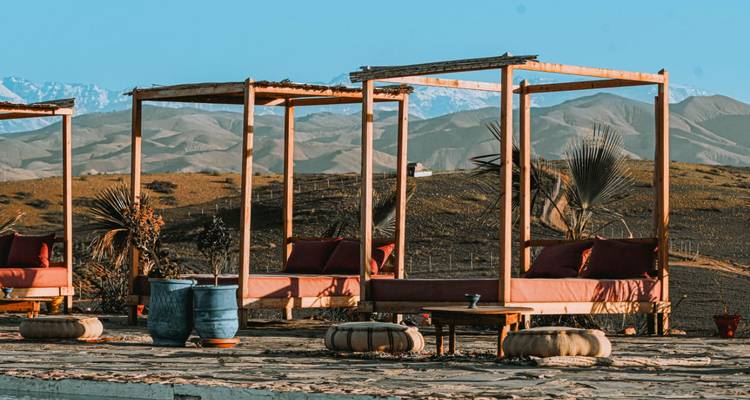 Stylish wooden cabanas with red cushions overlooking a rolling desert landscape and distant snow-capped mountains