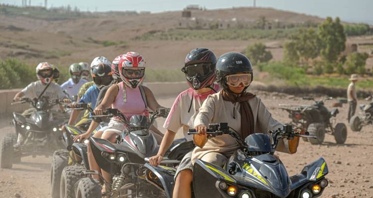 Line of travellers riding quad bikes through a dusty desert trail, all wearing helmets and goggles
