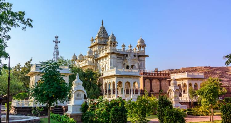 Elegantes Marmorkenotaph und Kuppeln von Jaswant Thada, umgeben von Grünflächen unter klarem Himmel.