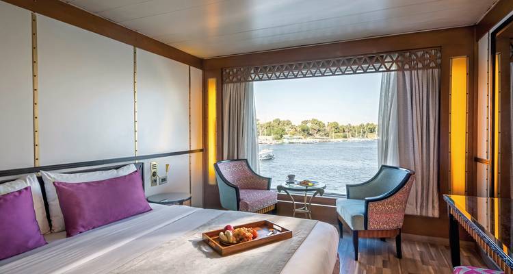 Helles Flussblick-Kajütchen mit großem Fenster, zwei Sesseln und einem ordentlich gemachten Bett an Bord eines Kreuzfahrtschiffes