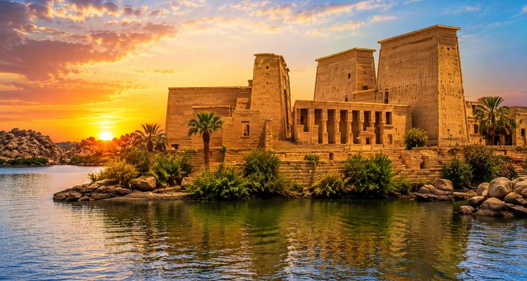 Temple of Philae sits on an island reflecting golden sunset hues across the Nile.