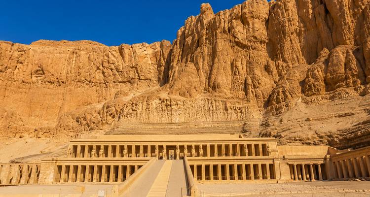 Temple of Hatshepsut carved beneath dramatic desert cliffs under a deep blue sky.