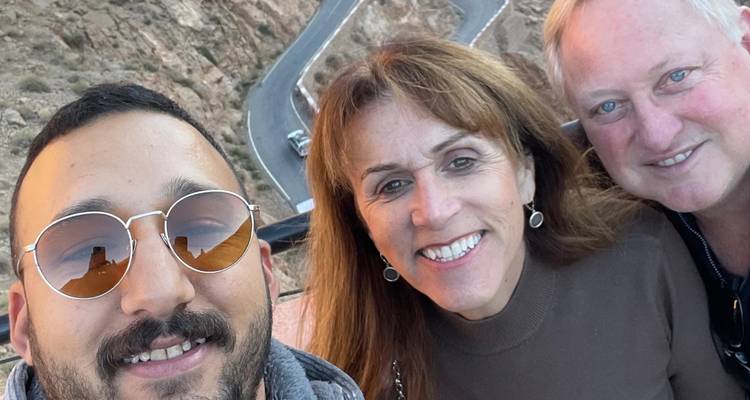 Selfie of three travelers smiling at a high viewpoint overlooking a winding cliff road.