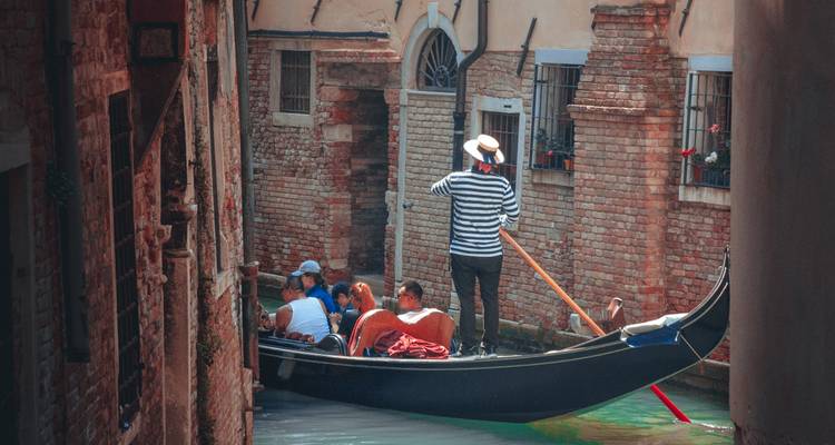 Un gondolier dirige une gondole transportant des touristes dans un canal étroit aux murs de briques