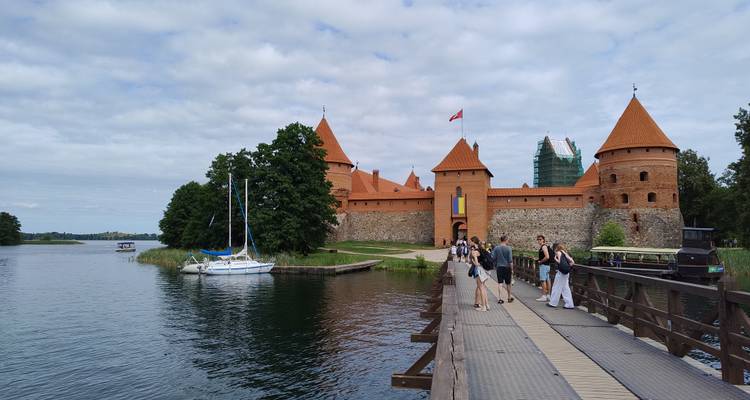 Visitors crossing wooden bridge toward red-roofed Trakai Island Castle over calm lake water.