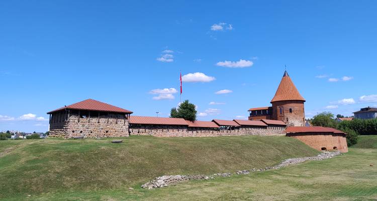 Medieval Kaunas Castle complex on grassy mound under bright blue sky with scattered clouds.
