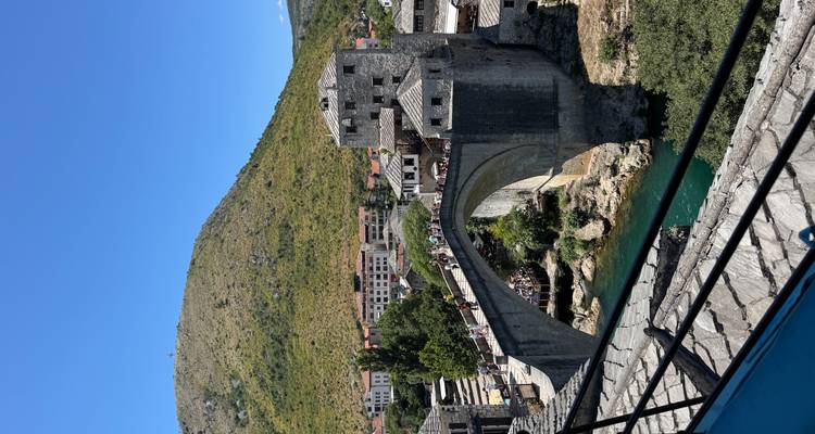 Vue latérale du pont en arc de pierre de Mostar rempli de touristes surplombant la rivière cristalline et les tours historiques.