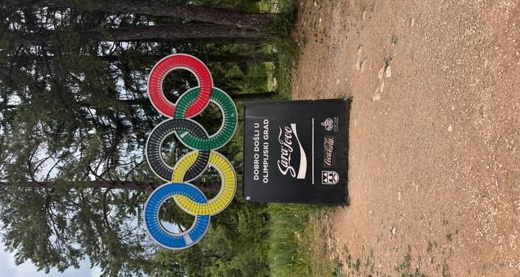 Sculpture aux anneaux olympiques colorés placée parmi les sapins accueillant les visiteurs dans la ville olympique.