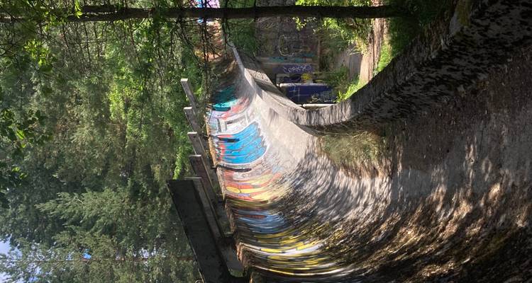 Section incurvée d'une piste de bobsleigh abandonnée baignée par la lumière du soleil avec des graffitis colorés tourbillonnant le long de ses murs.