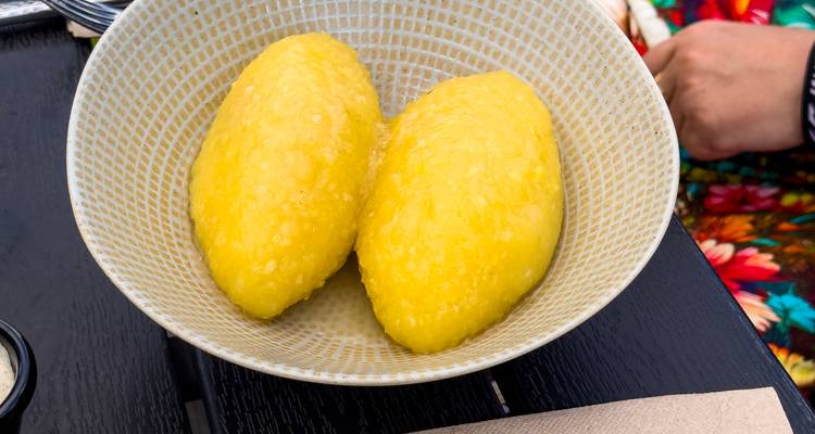 Gros plan de deux boulettes de pommes de terre jaune vif (cepelinai) servies dans un bol à motifs sur une table de restaurant.