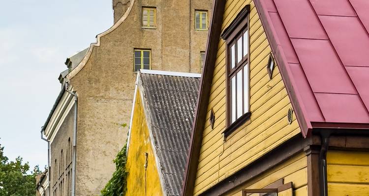 Des maisons en bois aux pignons colorés avec des toits jaunes et rouges juxtaposées à un bâtiment en pierre plus ancien.