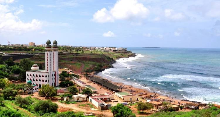 Une vue côtière surélevée montre une grande mosquée aux deux tours jumelles et des villages côtiers à côté des vagues turquoise de l'Atlantique.