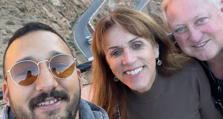 Selfie of three smiling travelers with winding mountain road far below them.