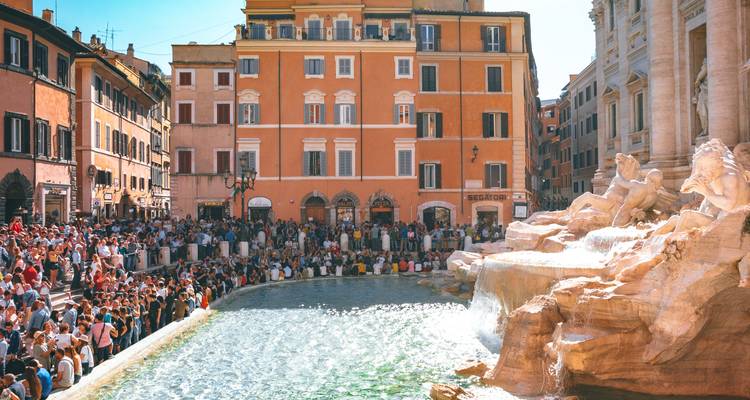 Large crowd gathered around Trevi Fountain as water cascades into the pool on a sunny day