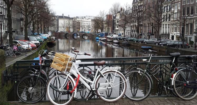 Des bicyclettes s'appuient contre la rampe d'un pont surplombant un canal paisible d'Amsterdam bordé de bateaux stationnés.