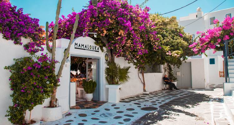Charming whitewashed alley in Mykonos lined with bright bougainvillea and a cozy restaurant entrance.