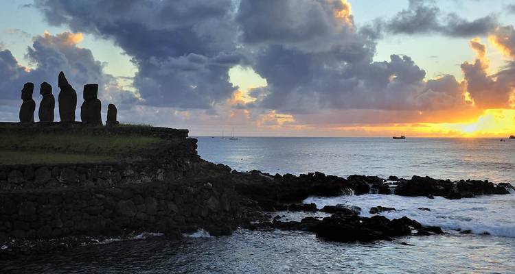 Silhouetted moai statues on a clifftop with a vivid ocean sunset on Easter Island.