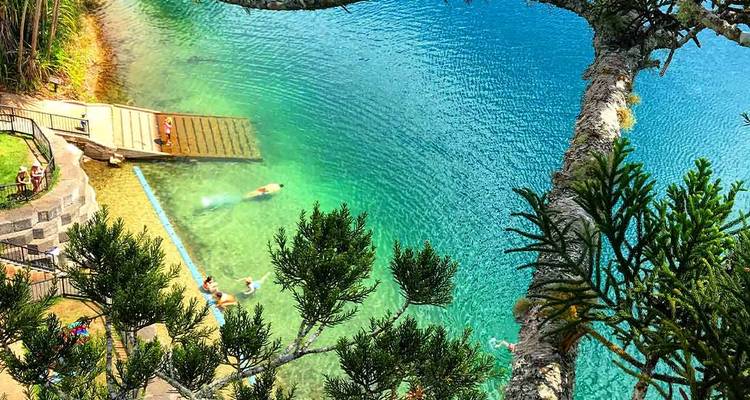Lac bleu aqua vu d'en haut avec des baigneurs et un ponton en bois entouré de verdure.