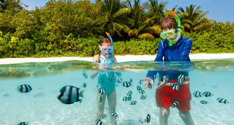 Dos niños bucean con tubo en aguas tropicales cristalinas rodeados de peces de arrecife rayados