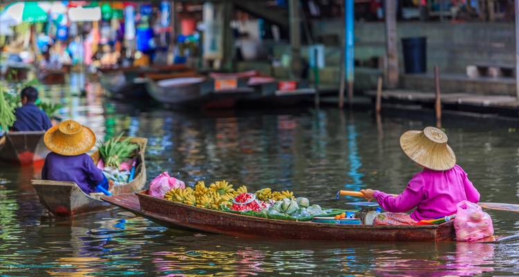 Vendedores con sombreros cónicos remando botes de madera cargados de productos frescos en un mercado flotante tailandés