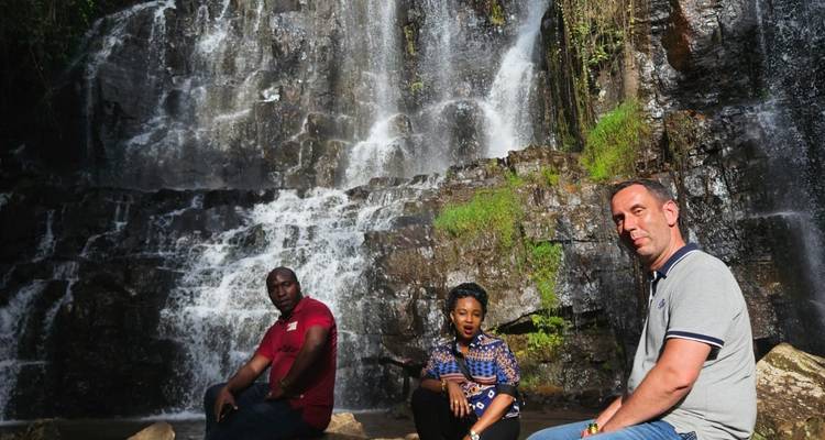 Three visitors sitting on rocks in front of a cascading tropical waterfall.