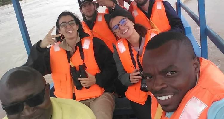 Selfie of smiling travelers wearing orange life vests aboard a small boat on a river.