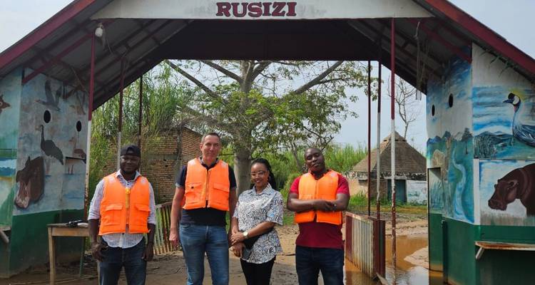 Group of visitors standing under the Rusizi entrance arch wearing bright life vests.