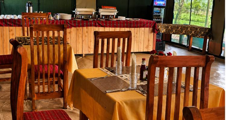 Cozy dining tent interior with wooden chairs and buffet setup overlooking the savanna.