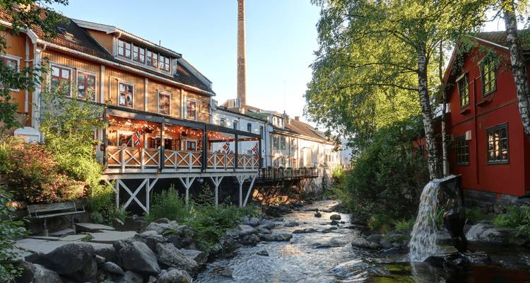 Charmante restaurantjes aan de rivier en houten gebouwen naast een kleine waterval in het avondlicht.