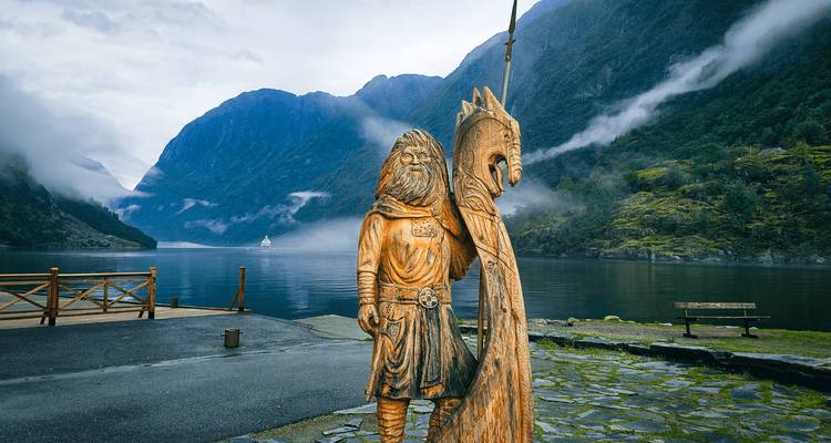 Houten Vikingse krijgerstandbeeld met uitzicht op mistige fjord met steile bergwanden.
