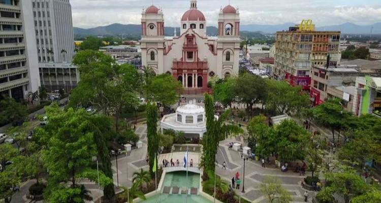 Place urbaine avec cathédrale à dôme précédée d'un parc aménagé et d'une fontaine