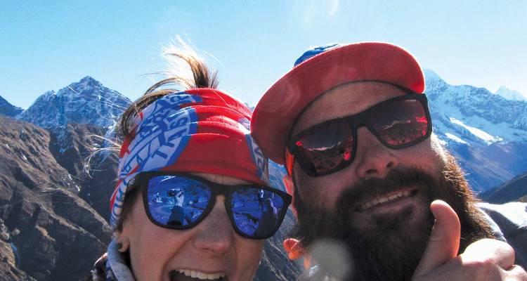 Selfie de cerca de dos excursionistas alegres usando gafas de sol con picos del Himalaya de fondo.