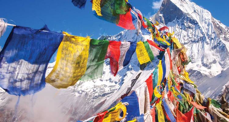 Las coloridas banderas de oración ondean contra un dramático pico del Himalaya cubierto de nieve.