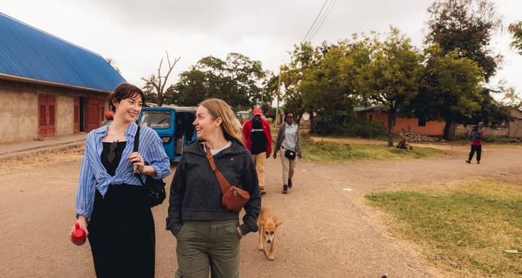 Travellers stroll through a rural village road chatting and smiling while locals walk behind them.