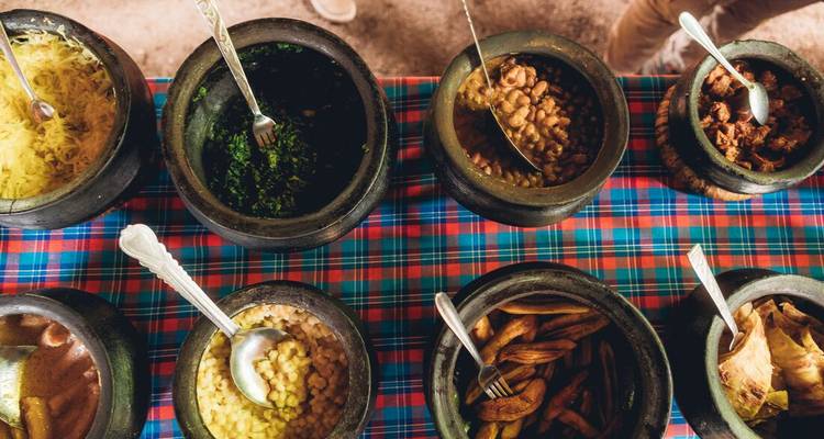 Colorful spread of traditional dishes served in clay pots on a checkered cloth.