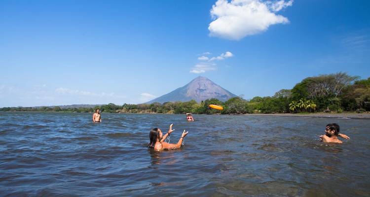 Des voyageurs se baignant et jouant au frisbee dans un lac d'eau douce avec un volcan se dressant au loin.