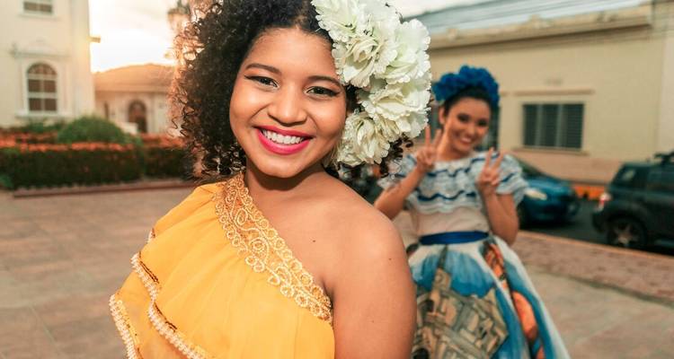 Des femmes souriantes vêtues de robes traditionnelles colorées posant avec entrain au coucher du soleil dans une cour coloniale.