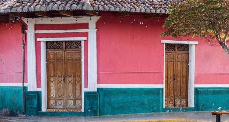 Simple colonial house facade painted vibrant pink with teal trim and two wooden doors.