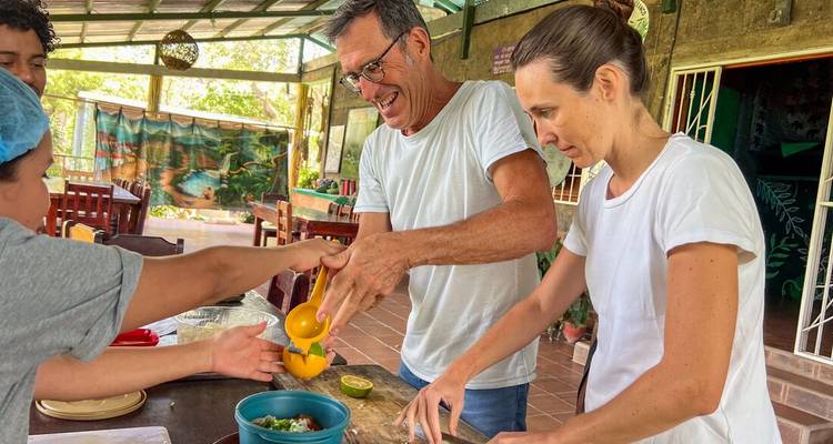 Visitors smiling and preparing food together during a hands-on cooking class in an open kitchen.