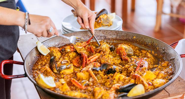 Gros plan d'une grande poêle de paëlla servie avec des fruits de mer, du riz et des quartiers de citron