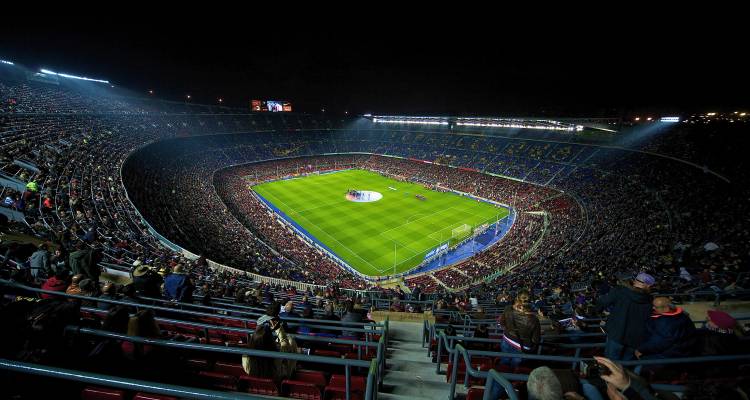 Vue aérienne élevée du stade Camp Nou bondé lors d'un match de football nocturne avec un terrain vert éclatant.